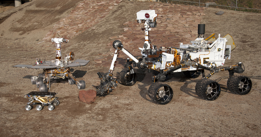 The setting is JPL&#039;s Mars Yard testing area. Front and centre: flight spare for the first Mars rover, Sojourner, which landed on Mars in 1997 as part of the Mars Pathfinder Project. Left: a Mars Exploration Rover Project test rover that is a working sibling to Spirit and Opportunity, which landed on Mars in 2004. Right: a Mars Science Laboratory test rover the size of that project&#039;s Mars rover, Curiosity,