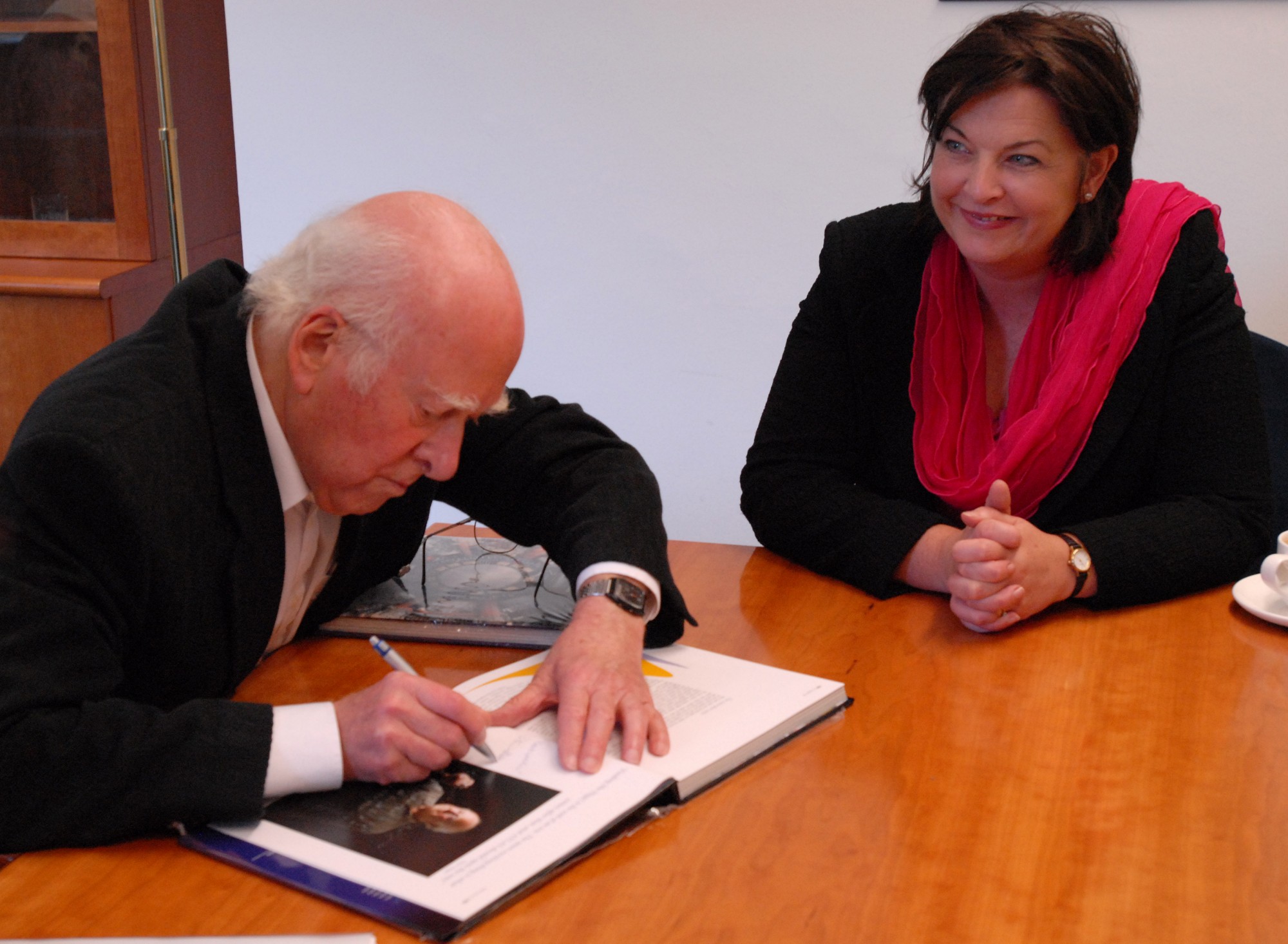 Peter Higgs autographing the ATLAS book &#039;Exploring the Mystery of Matter&#039; presented to Fiona Hyslop, on the right.