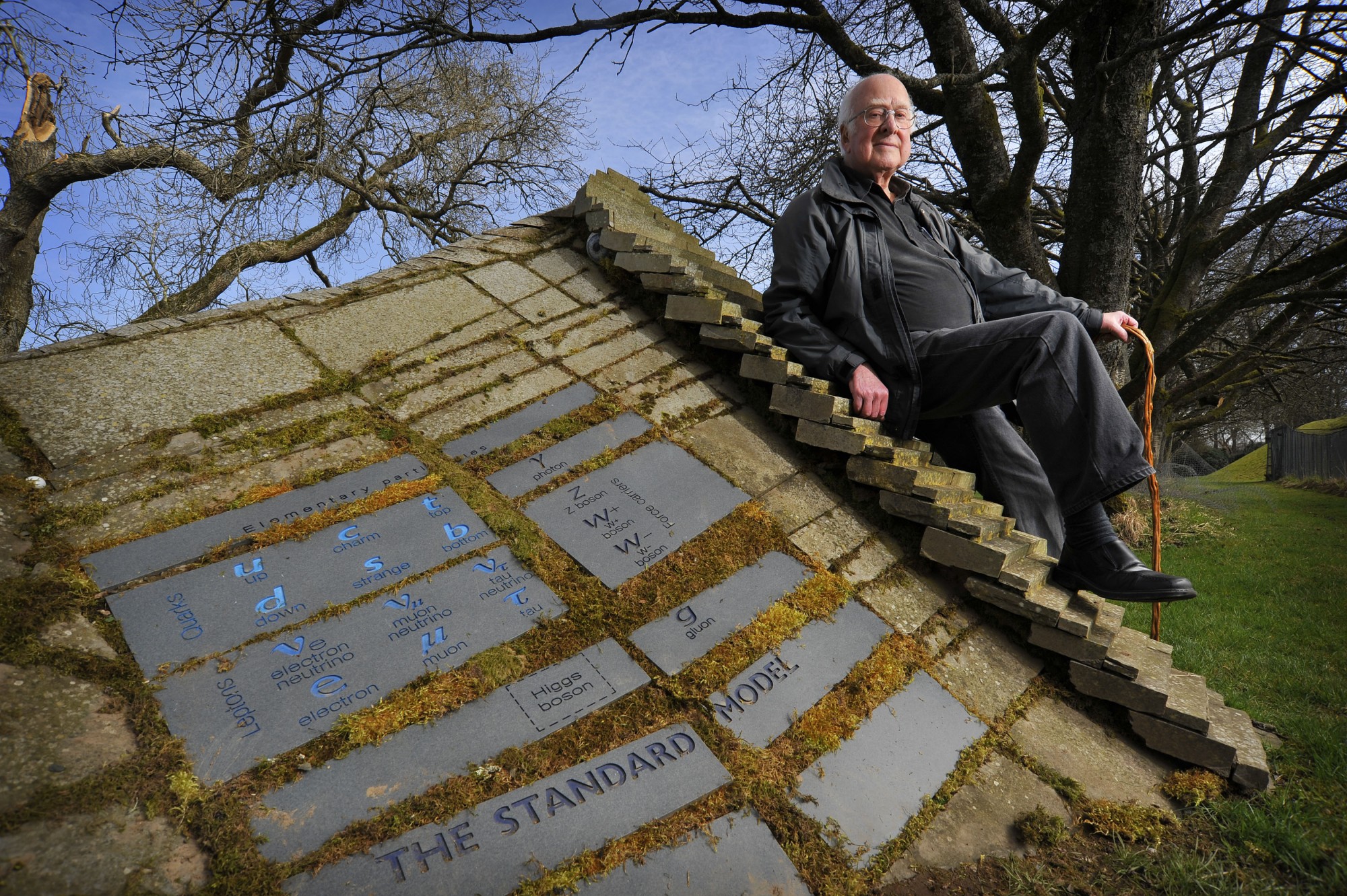 Peter Higgs resting against the Standard Model landscape sculpture that includes the Higgs Boson.