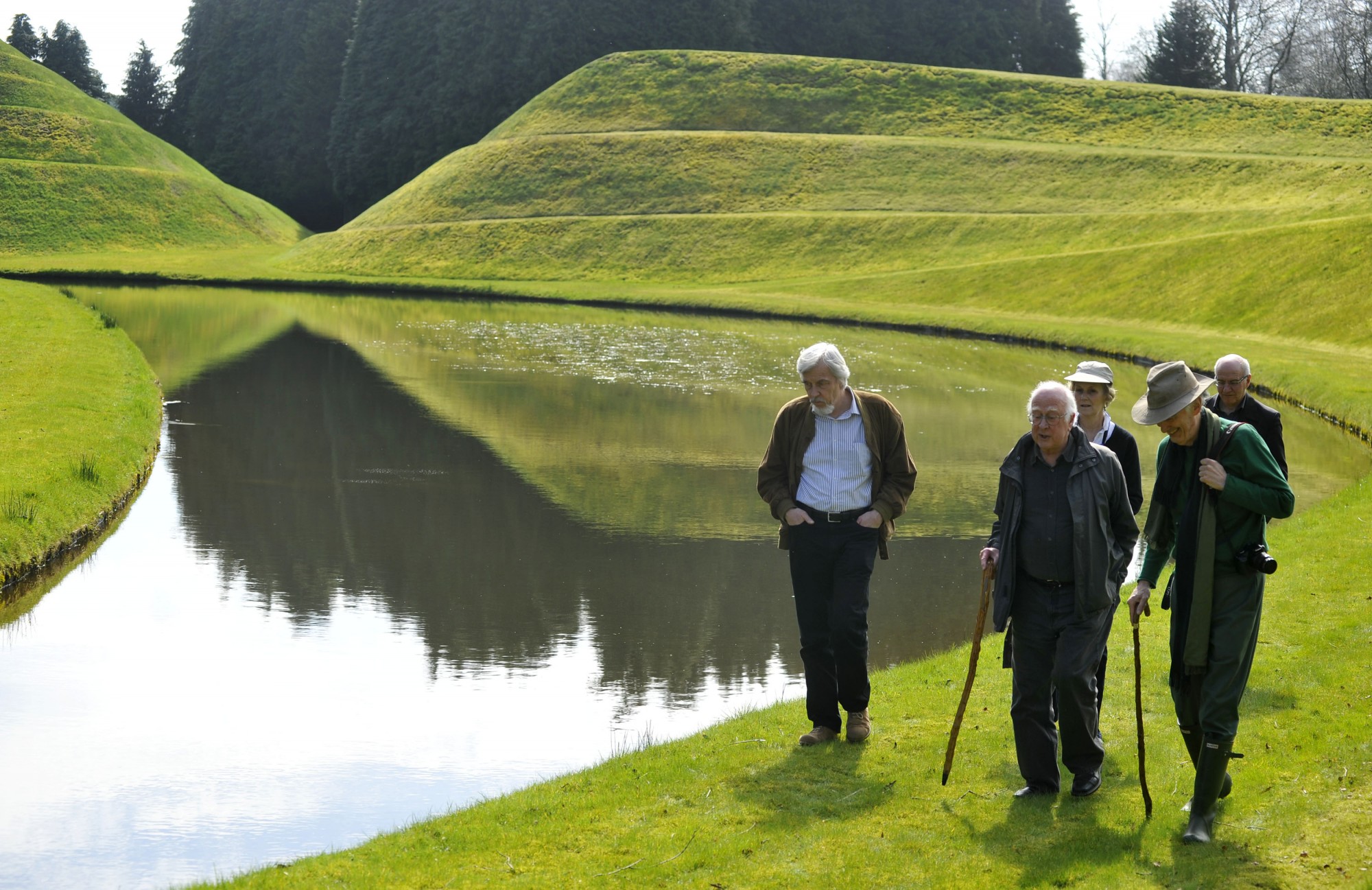 Left to right: Rolf Heuer, Peter Higgs and Charles Jencks walk alongside one of the garden&#039;s artificial lakes. Behind are James Gillies and Alan Walker. In the background on the left is the &#039;double helix&#039; mound.