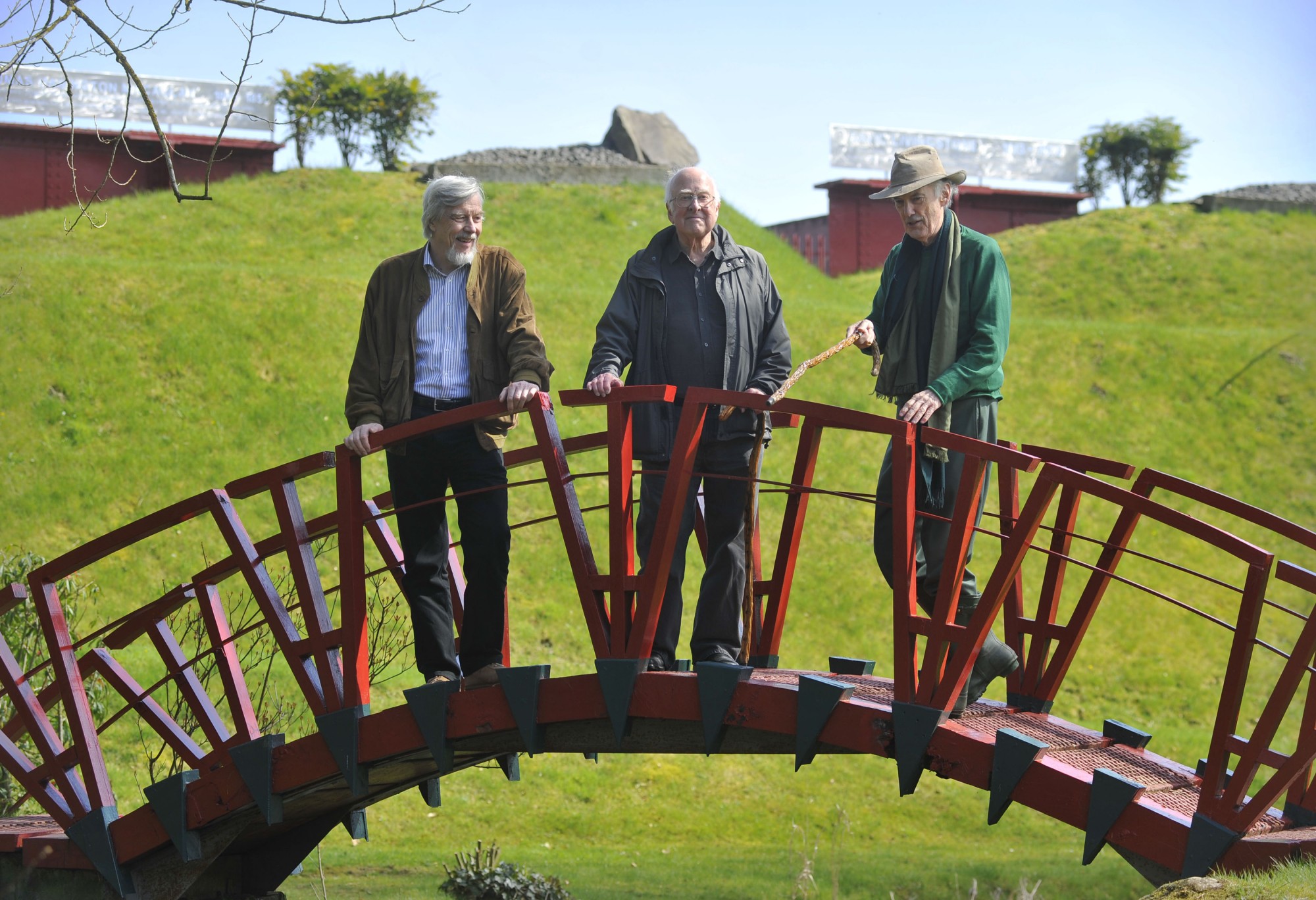 Left to right: Rolf Heuer, Peter Higgs and Charles Jencks standing on a bridge over one of the garden&#039;s water channels.